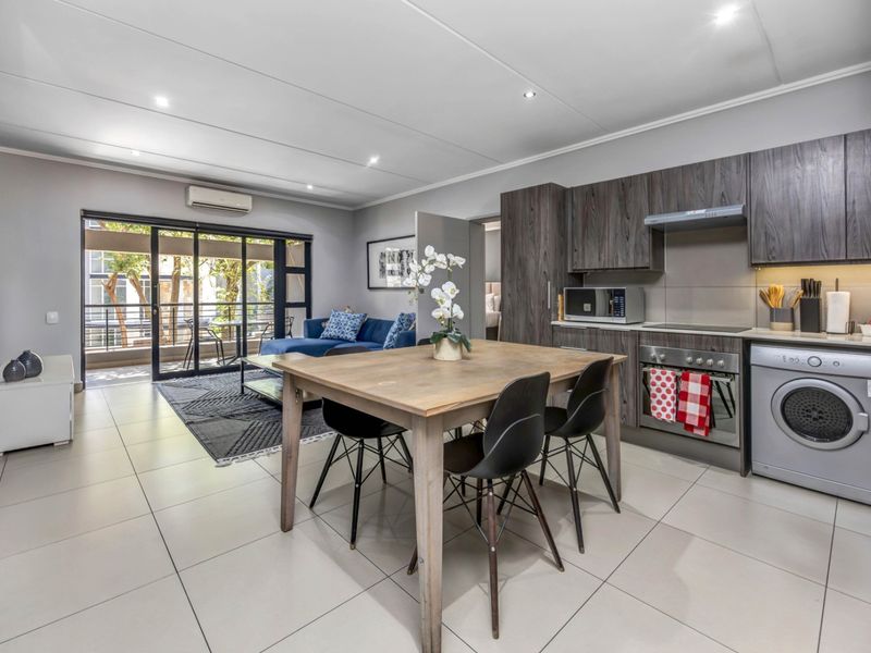 Modern open-plan living area featuring a contemporary kitchen with built-in appliances, tiled flooring, and seamless access to a private balcony.