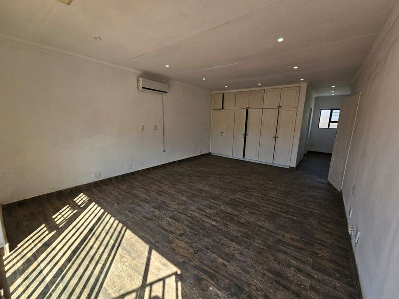Spacious bedroom featuring wood-look tile flooring, built-in cupboards, and a wall-mounted air conditioning unit with recessed lighting.
