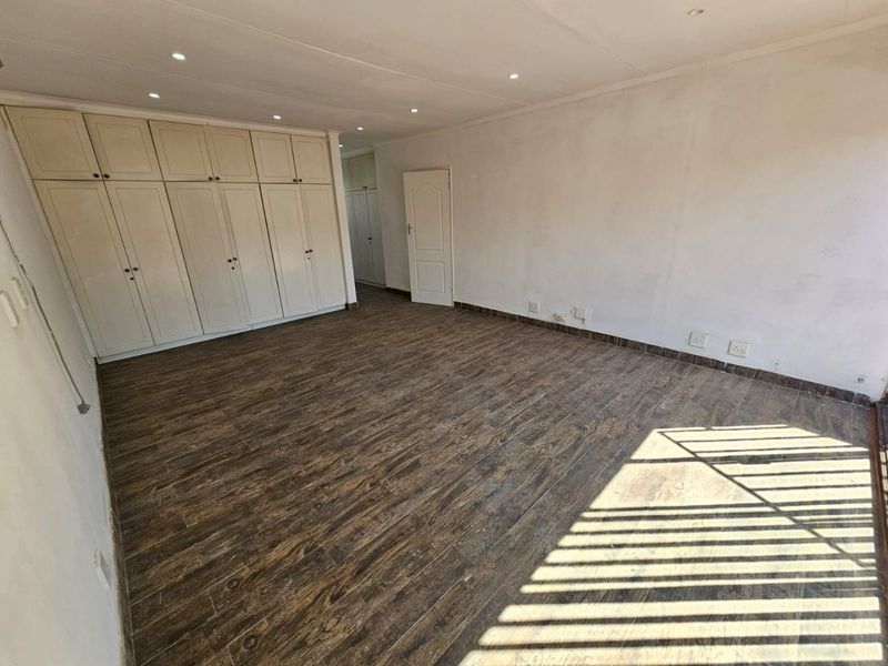 Spacious bedroom featuring extensive built-in cupboards, wood-look tile flooring, and recessed downlighting, offering a blank canvas for personalization.
