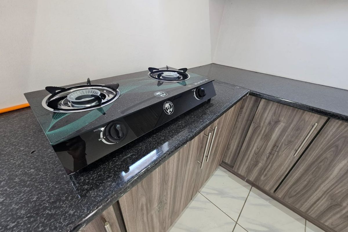 A modern kitchen corner featuring dark granite countertops, wood-grain laminate cabinetry, and a built-in gas hob on a tiled floor.
