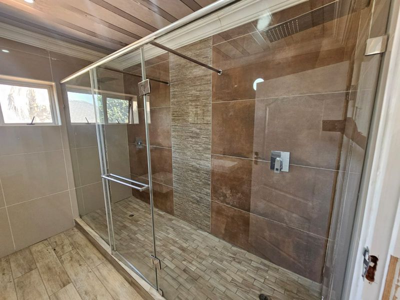 Modern walk-in shower featuring a glass enclosure, rain shower head, and decorative tiled wall accents with a timber ceiling.