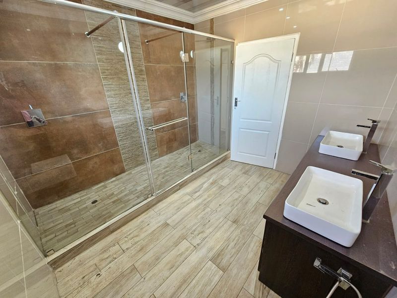 Modern bathroom featuring a spacious walk-in shower with glass enclosure and a double vanity with contemporary vessel sinks.
