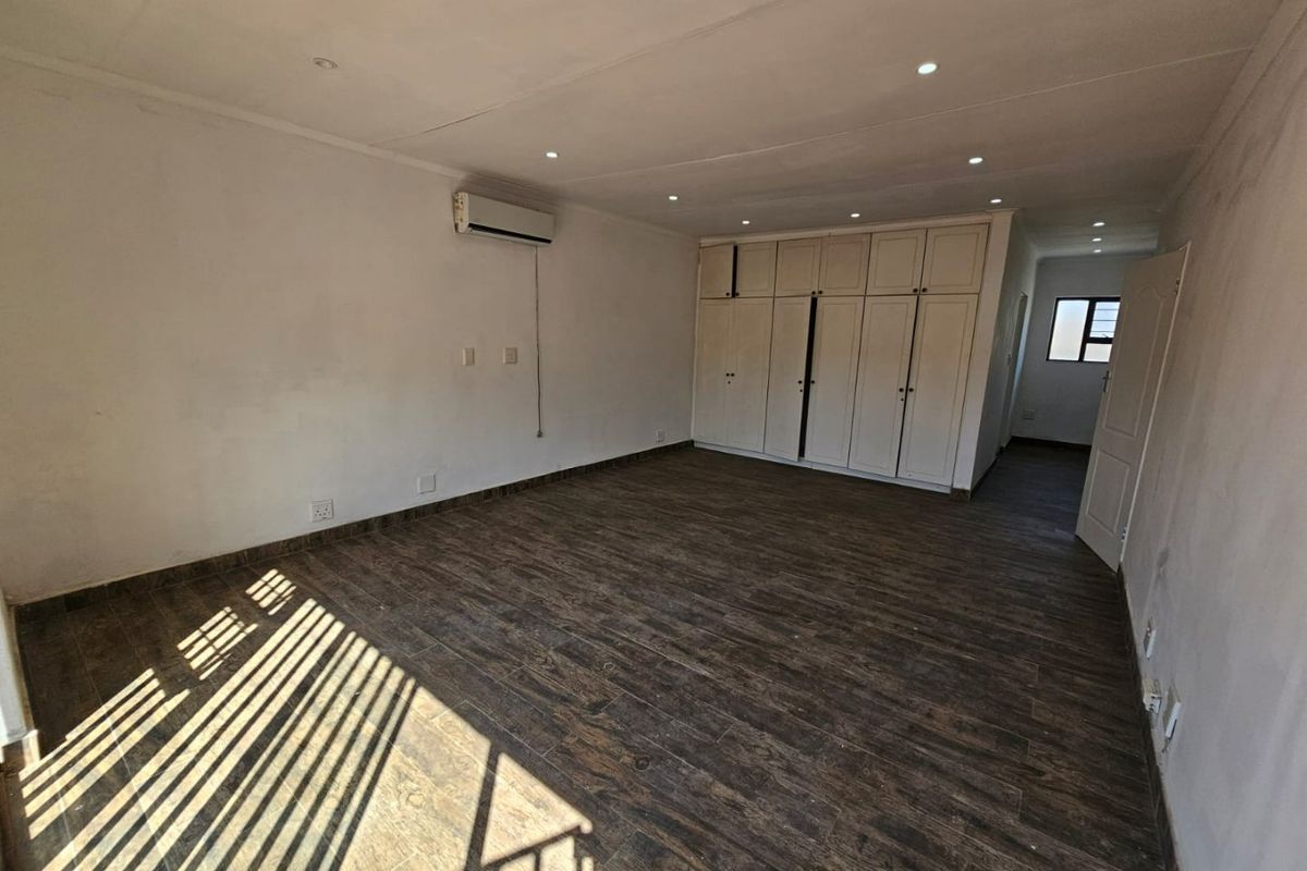 Spacious bedroom featuring dark wood-look tiled flooring, extensive built-in cabinetry, recessed lighting, and a wall-mounted air conditioning unit.