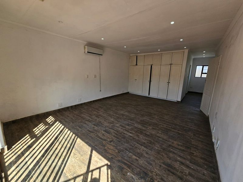 Spacious bedroom featuring dark wood-look tiled flooring, extensive built-in cabinetry, recessed lighting, and a wall-mounted air conditioning unit.