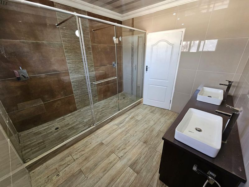 Modern bathroom featuring a spacious walk-in shower with glass enclosure, double vanity with vessel sinks, and contemporary tiled finishes.