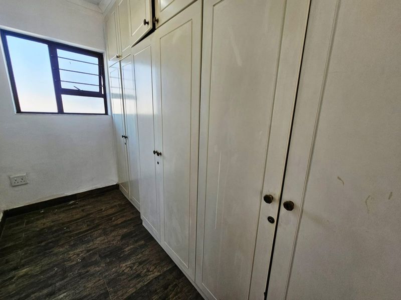 A bedroom featuring extensive built-in cupboards, dark laminate flooring, and a window providing natural light.