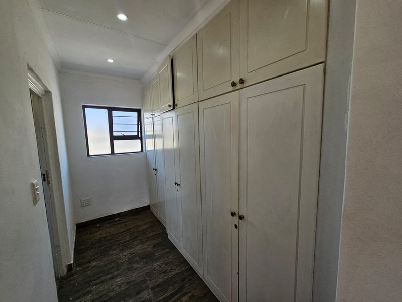 A functional hallway featuring extensive built-in floor-to-ceiling storage cupboards, tiled flooring, and recessed downlighting.