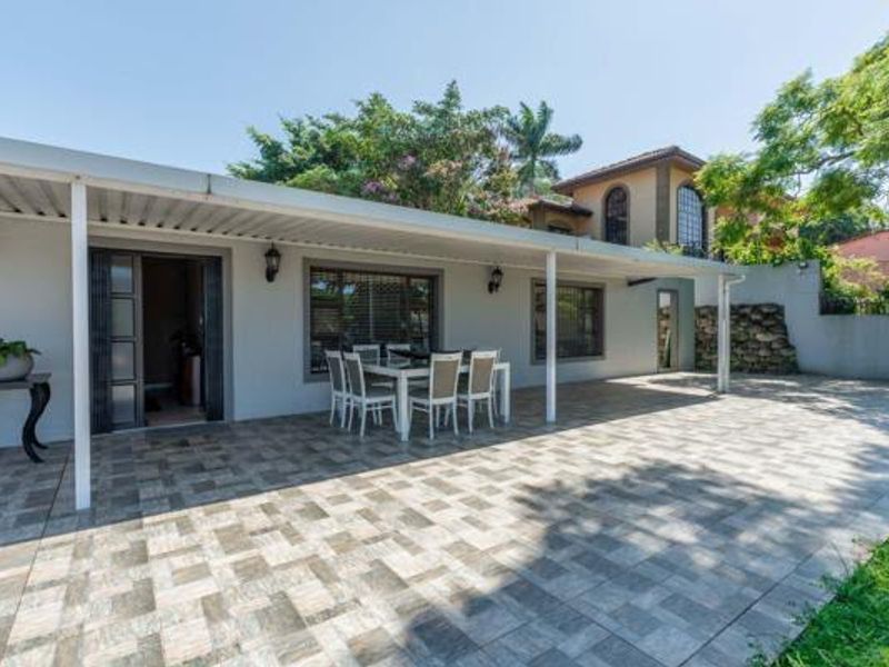 A spacious covered patio featuring tiled flooring and wall-mounted lighting, providing an ideal outdoor entertainment area overlooking the garden.
