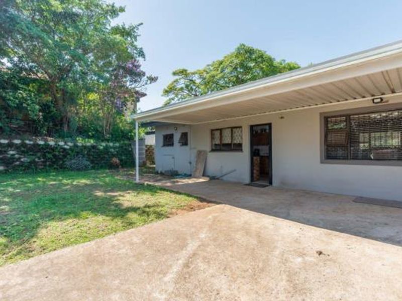 Rear view of the property featuring a covered concrete patio, established garden, and retaining wall, providing a functional outdoor living space.