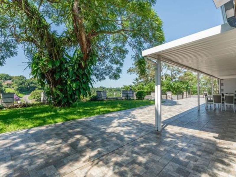 Spacious covered patio featuring tiled flooring and metal structural supports, overlooking a landscaped garden and scenic neighborhood views.