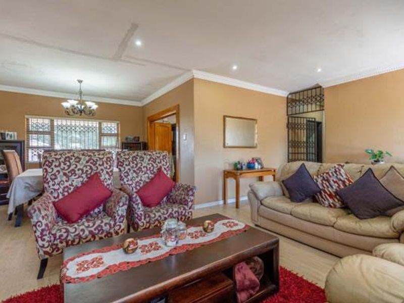 Spacious living room featuring laminate flooring, recessed downlighting, and decorative coving, with a security gate leading to an adjacent area.