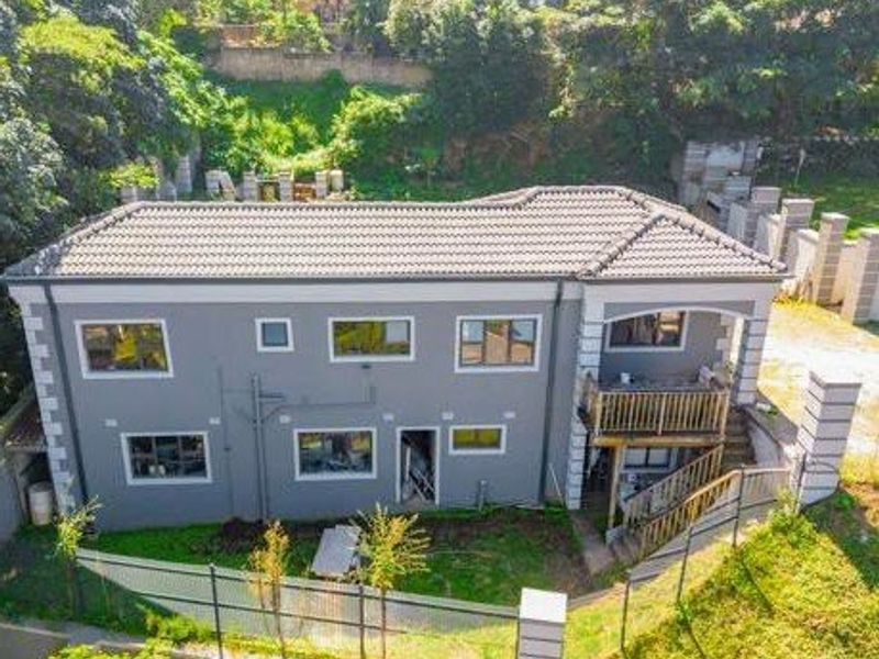 Aerial view of a two-story residential property featuring a tiled roof, timber balcony, and exterior staircase, set within a sloped garden area.