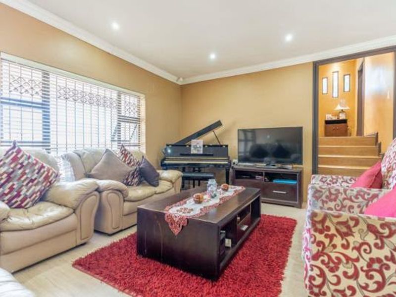 A comfortable living room featuring tiled flooring, recessed downlighting, and security bars on the windows, with an open transition to the staircase area.