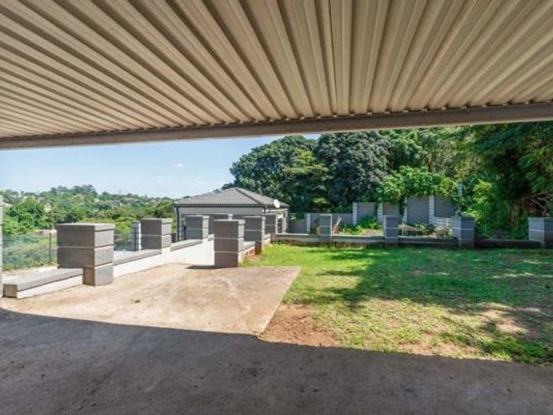 A spacious covered patio overlooking a private garden with masonry boundary walls and established trees in the background.