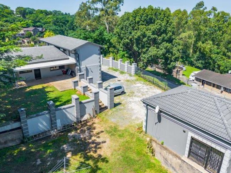 Aerial view of the property showing the main dwelling, secondary structure, boundary walls, and surrounding landscaped grounds.