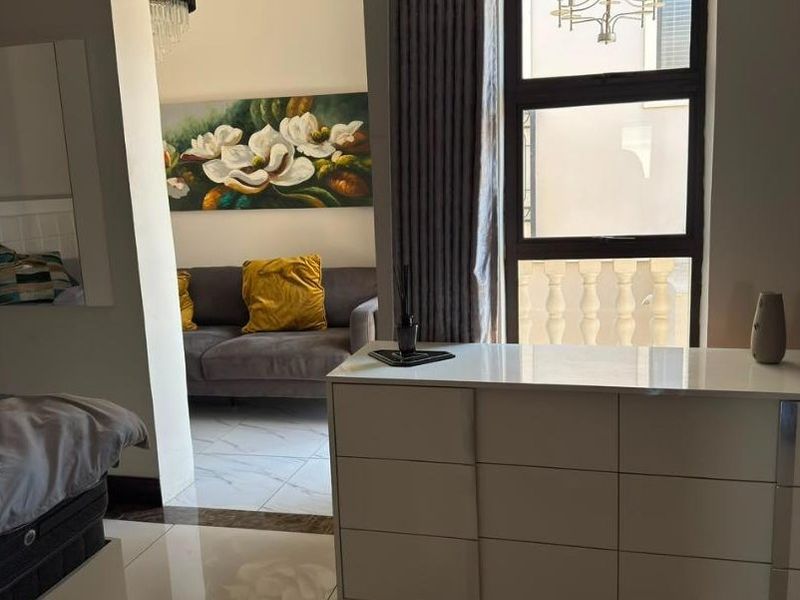 A well-maintained bedroom featuring polished tiled flooring, modern aluminium window frames, and a neutral color palette with a view into an adjacent living area.