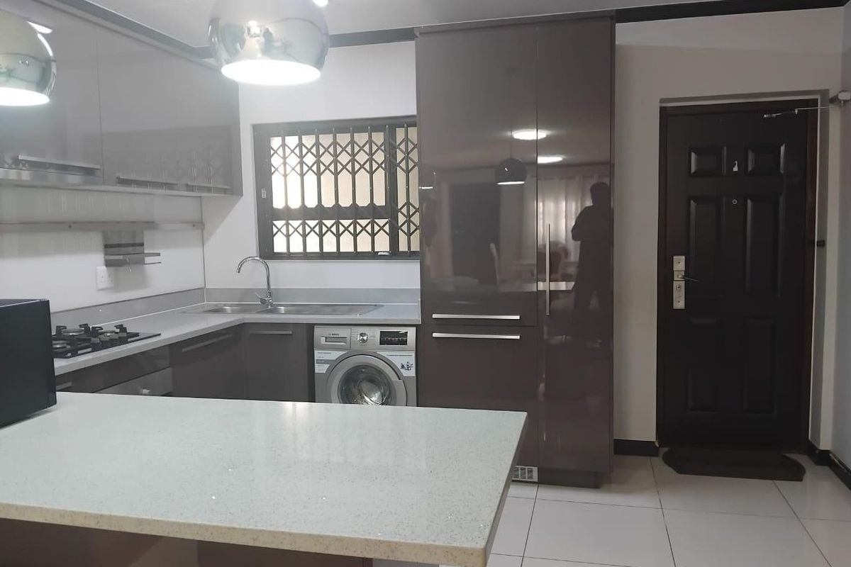 Modern kitchen featuring high-gloss cabinetry, stone countertops, a gas hob, and integrated laundry facilities with tiled flooring and direct exterior access.