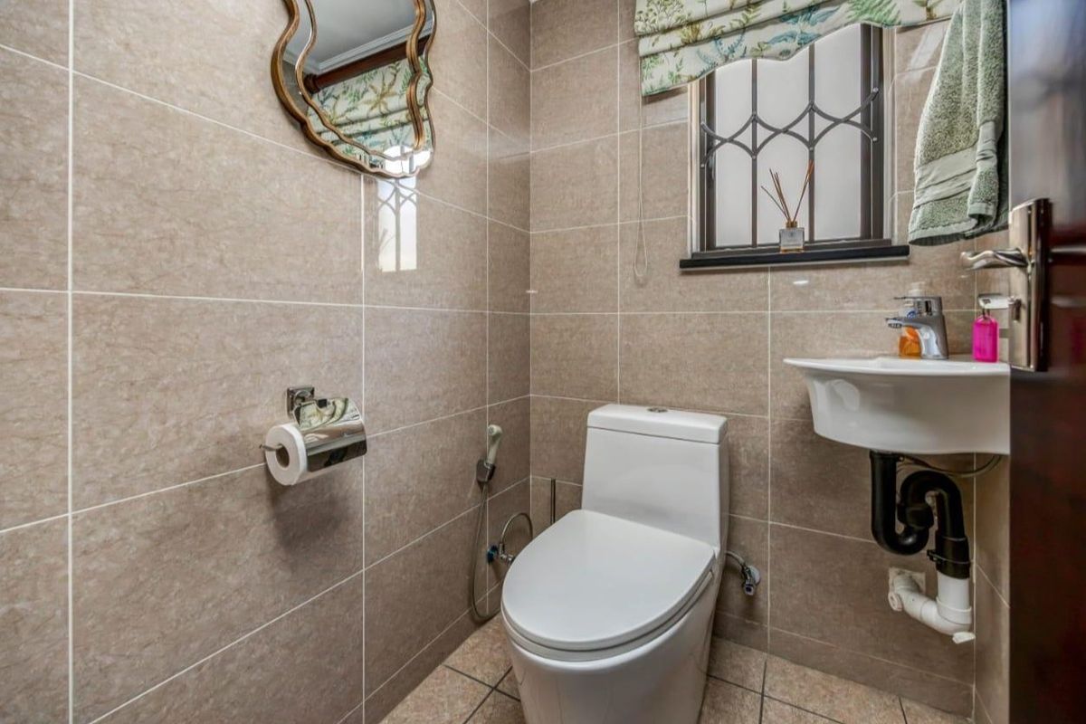 A compact, well-maintained bathroom featuring floor-to-ceiling beige tiling, a modern toilet, and a wall-mounted basin with exposed plumbing.