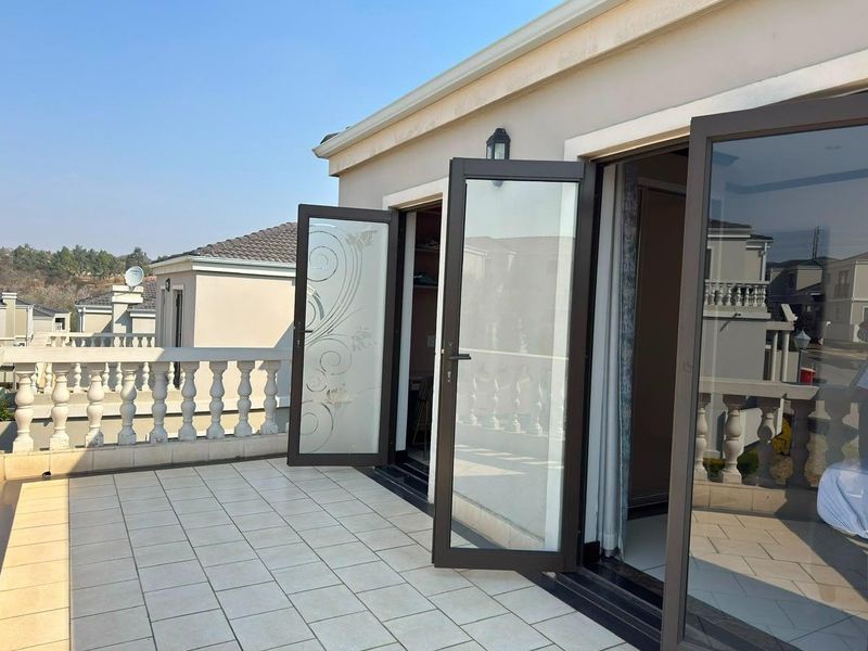A spacious tiled balcony featuring a decorative balustrade and double glass doors providing access to the interior living space.