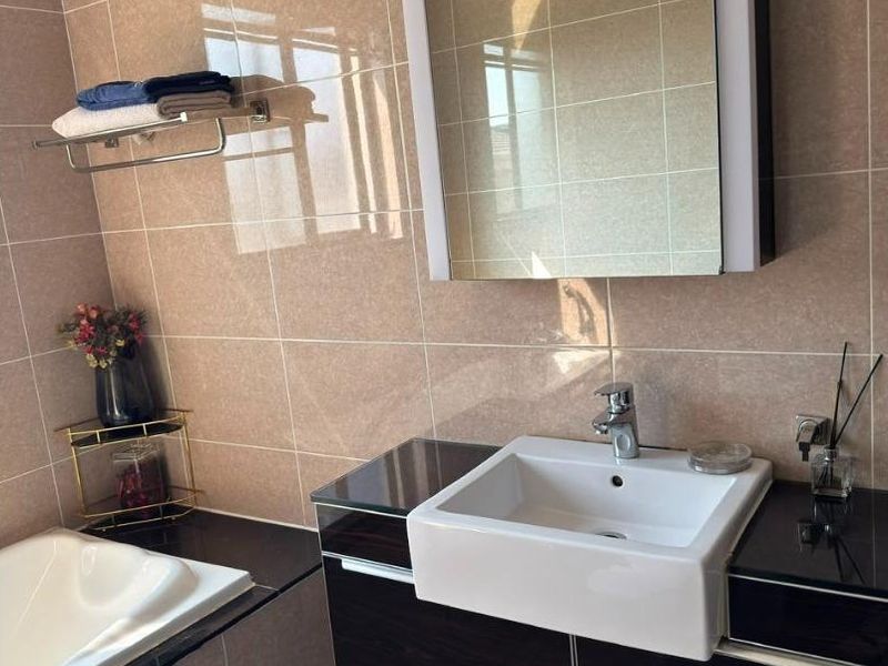 A modern bathroom featuring a built-in vanity with a ceramic basin, wall-mounted mirror cabinet, and tiled finishes throughout.