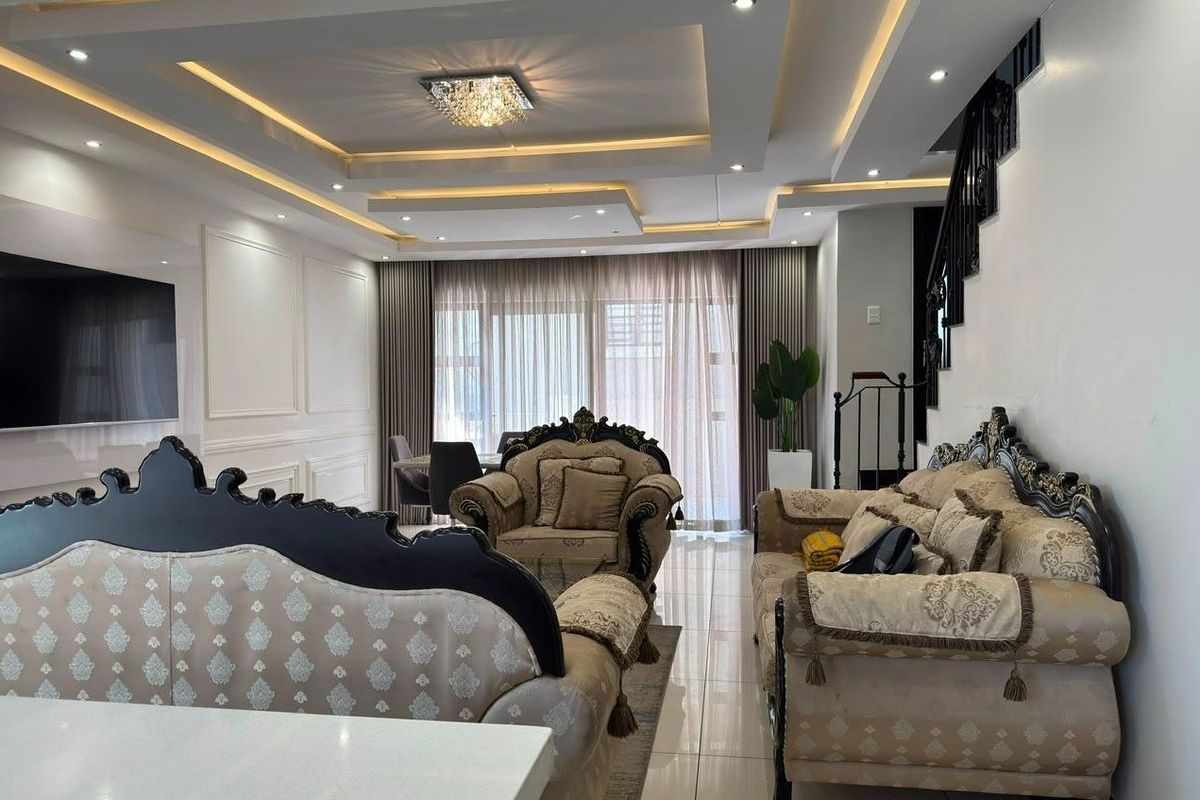 Spacious living area featuring a modern recessed tray ceiling with integrated lighting, elegant wainscoting, and polished floor tiles.