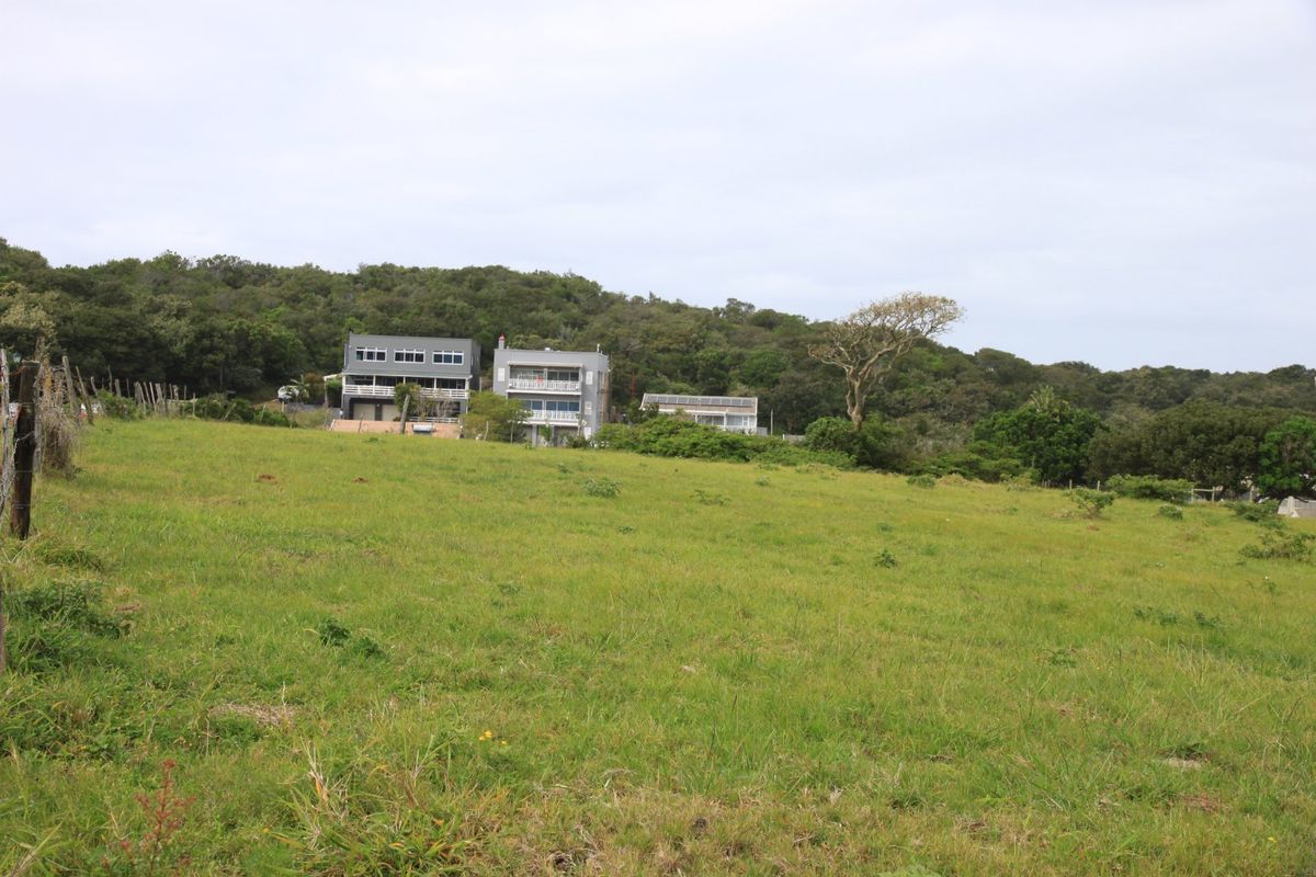 A view of a vacant residential plot featuring grassy terrain and perimeter fencing, with neighboring properties visible in the background.
