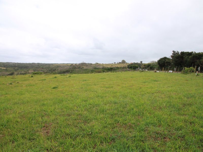 A wide, open grassy plot of vacant land featuring natural landscape views and perimeter wire fencing.
