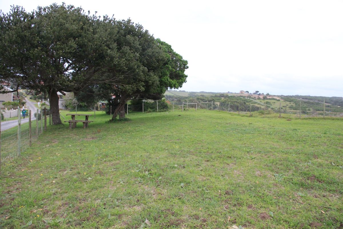 A spacious, grassy vacant residential plot featuring mature trees and perimeter wire mesh fencing, offering a natural setting for potential development.