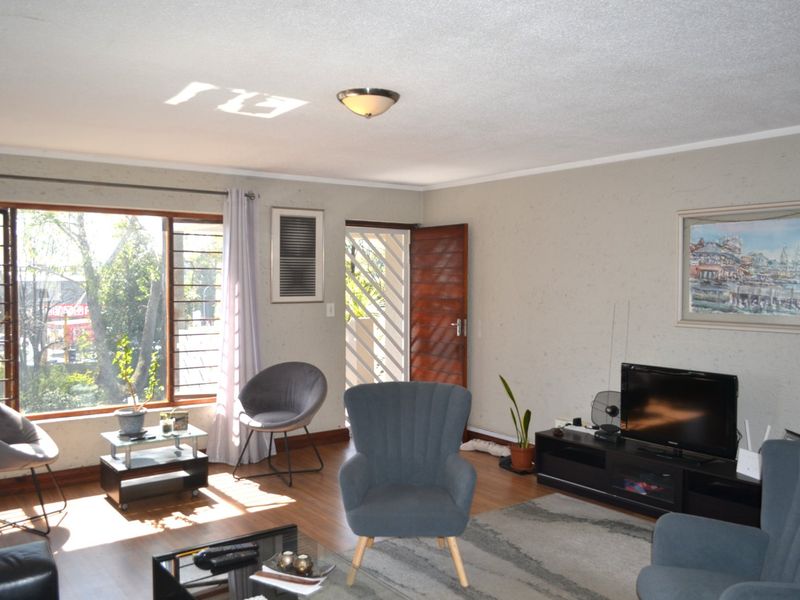 A bright living room featuring laminate flooring, large windows providing natural light, and direct access to an exterior security gate.