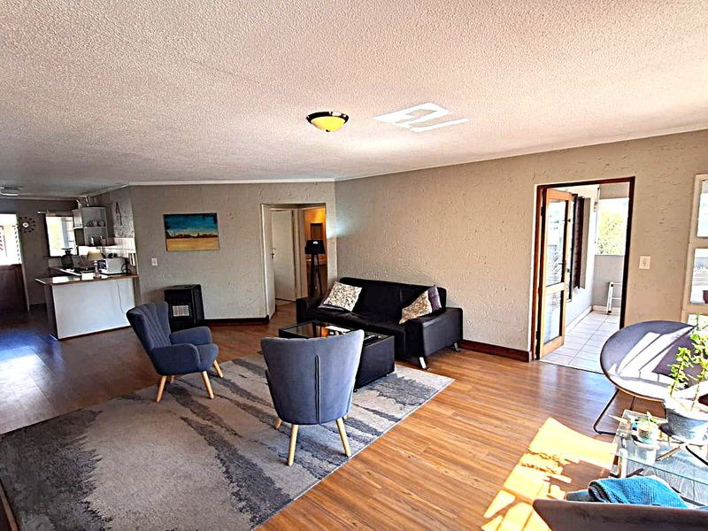 Spacious open-plan living area featuring laminate flooring, textured walls, and an integrated kitchen space with direct access to an outdoor patio.