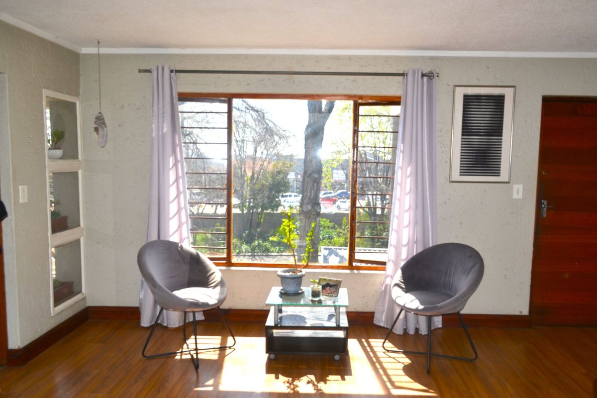 A living room featuring timber flooring, a large window with security bars, and a built-in wall niche, offering natural light and a view.