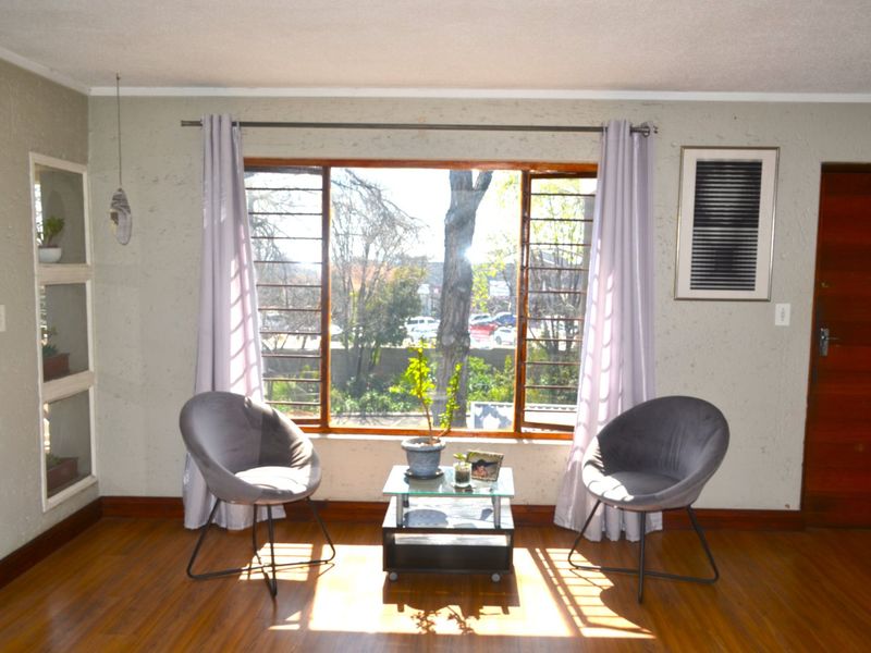 A living room featuring timber flooring, a large window with security bars, and a built-in wall niche, offering natural light and a view.