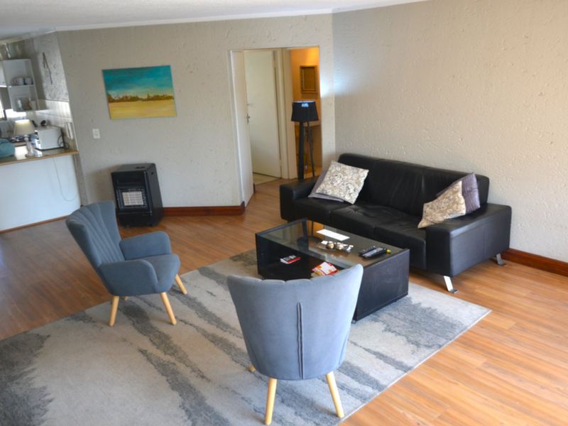 Open plan living area featuring laminate flooring, a gas heater, and an adjacent kitchen space with built-in cabinetry.