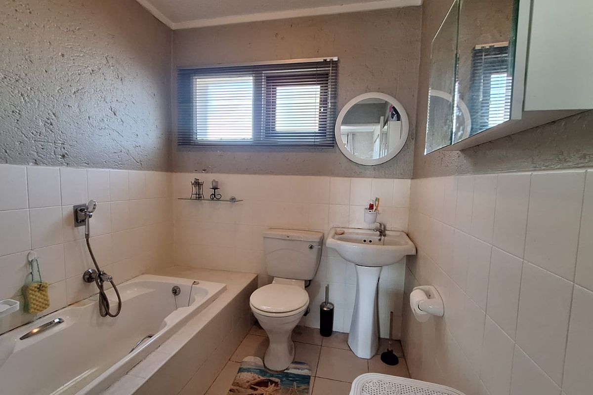 A functional bathroom featuring a bathtub, pedestal basin, and toilet with tiled finishes, offering potential for cosmetic updates to modernize the space.