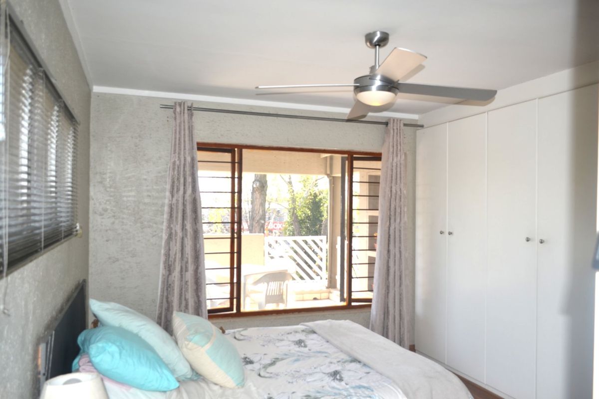 A bedroom featuring built-in cupboards, a ceiling fan, and security bars on the window, with direct access to an outdoor balcony area.