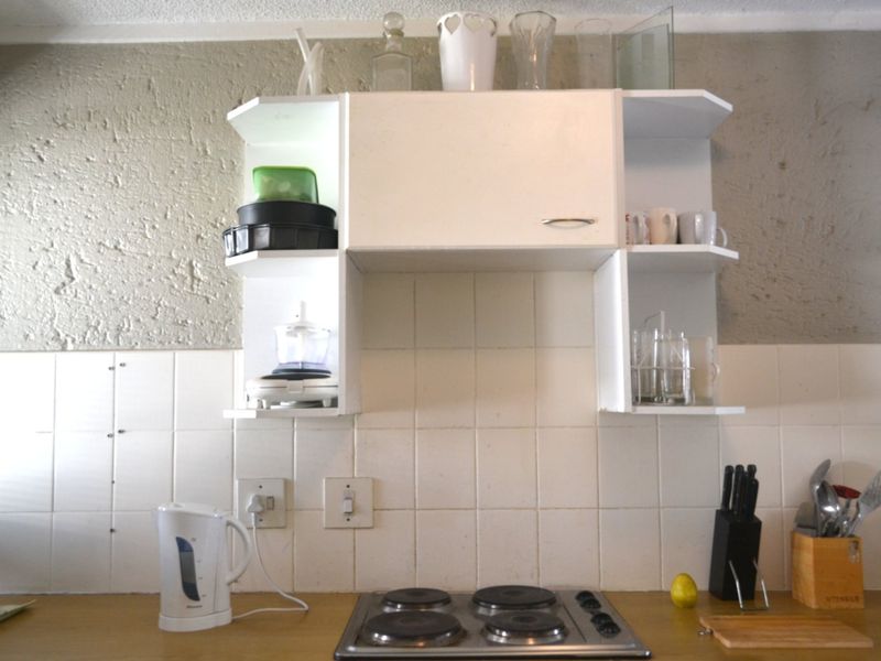 A compact kitchen area featuring a built-in electric hob, tiled splashback, and overhead cabinetry with open shelving.