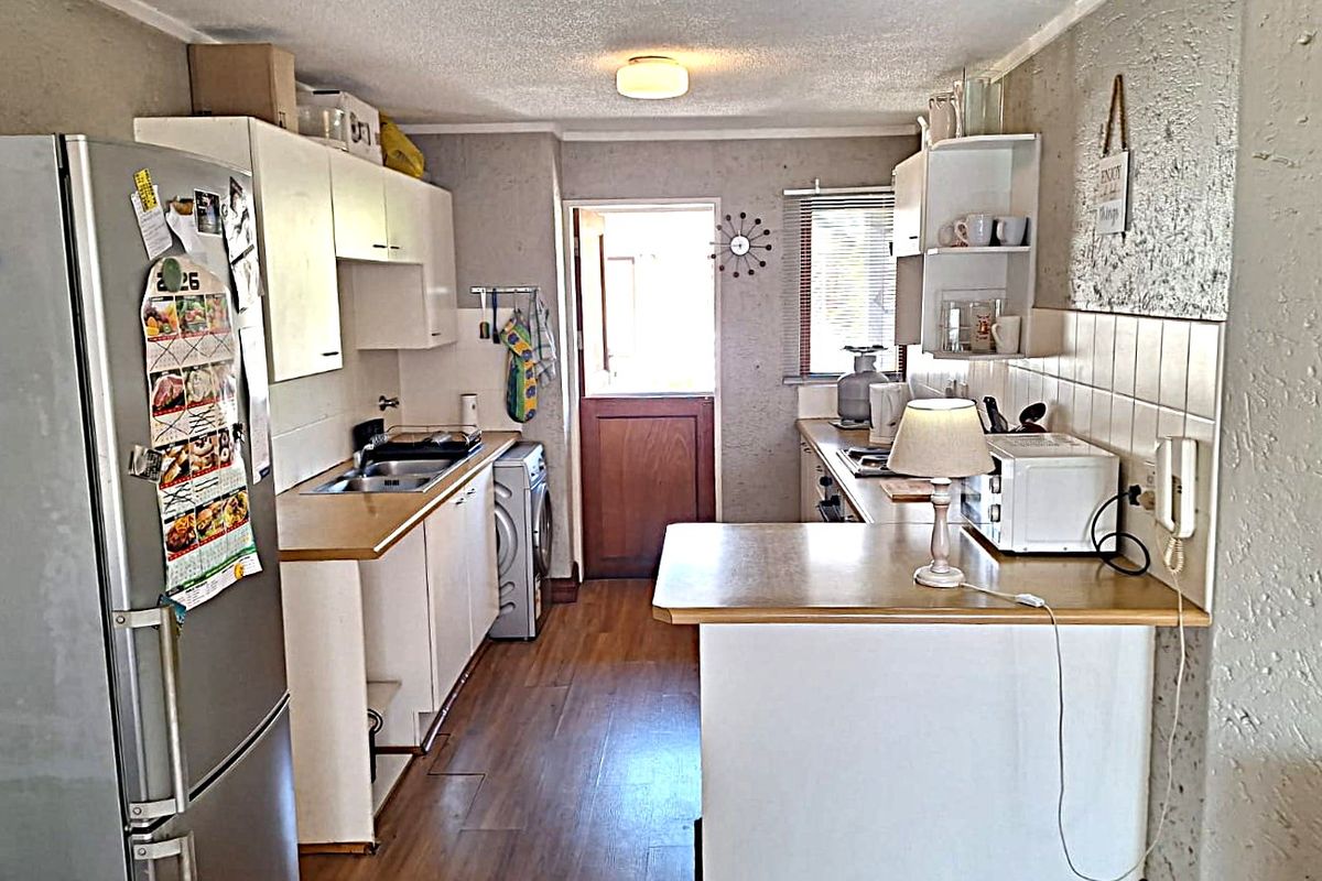 A functional kitchen featuring laminate countertops, built-in cabinetry, a tiled backsplash, and integrated laundry plumbing with direct access to the exterior.