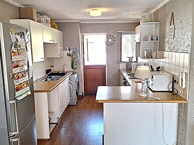 A functional kitchen featuring laminate countertops, built-in cabinetry, a tiled backsplash, and integrated laundry plumbing with direct access to the exterior.