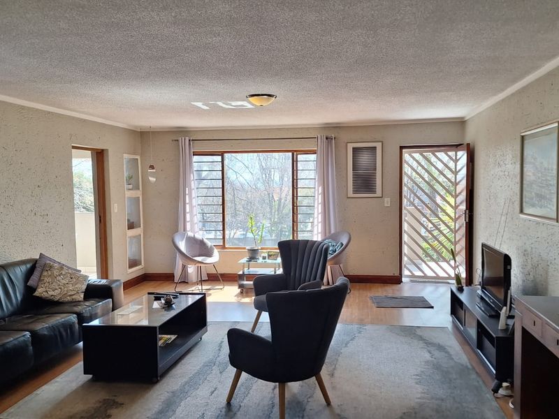 A spacious living room featuring textured walls, large windows providing natural light, and direct access to an exterior area through a security gate.