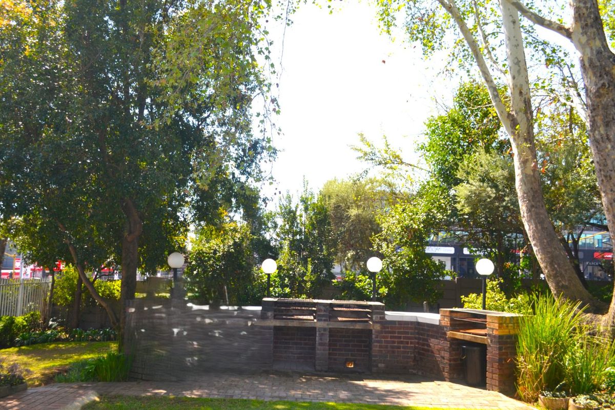 A private outdoor garden area featuring a built-in brick braai and paved entertainment space surrounded by mature trees and established landscaping.