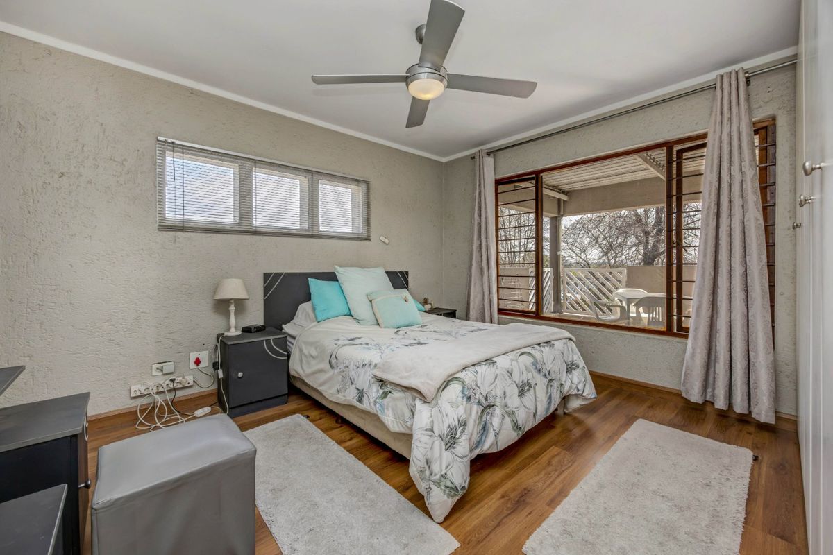 A well-lit bedroom featuring laminate flooring, a ceiling fan, and large windows with access to an outdoor balcony area.