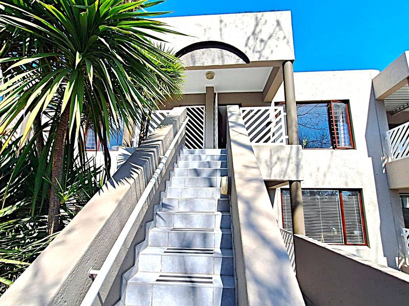 Exterior view of an apartment building entrance featuring a tiled staircase with metal balustrades and security-fitted windows.