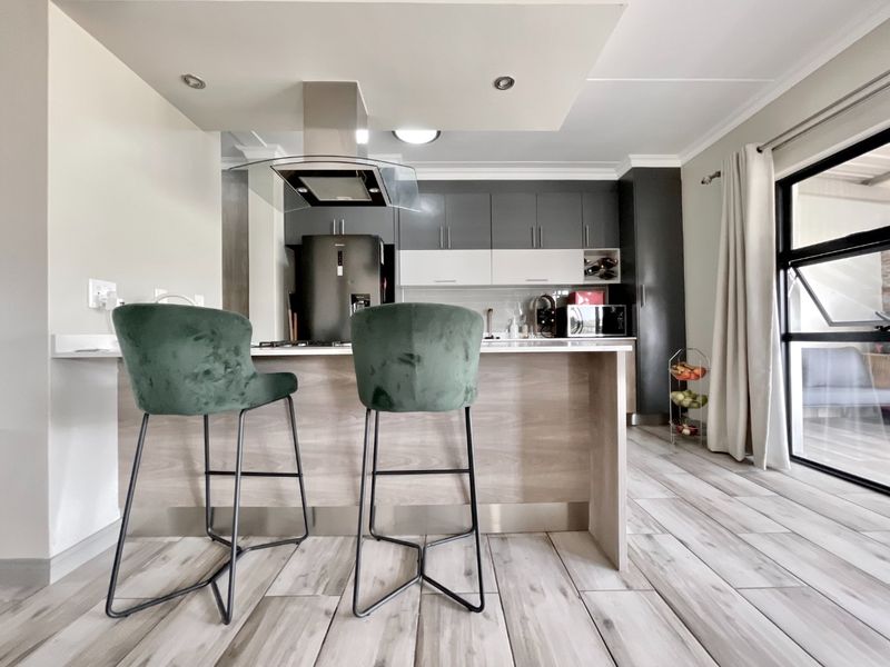 Modern kitchen featuring a central island with breakfast bar, sleek two-tone cabinetry, stainless steel extractor fan, and light wood-look tiled flooring.