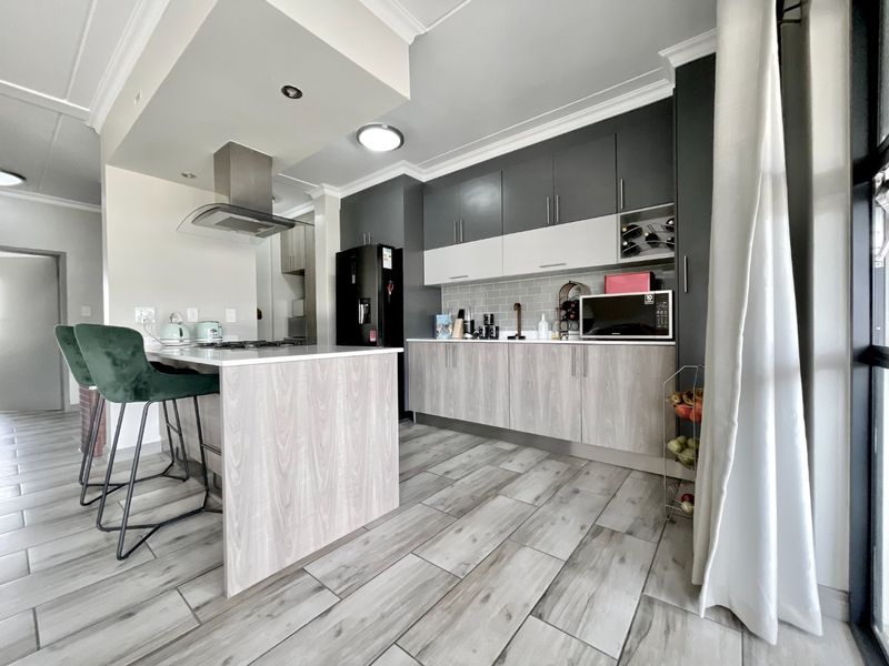 Modern kitchen featuring two-tone cabinetry, a central island with breakfast bar, subway tile backsplash, and contemporary wood-look tile flooring.