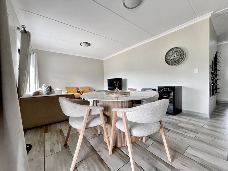 An open-plan living and dining area featuring modern wood-look tiled flooring, neutral wall tones, and clean architectural finishes.