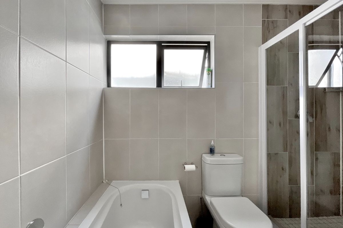 A modern bathroom featuring a built-in bathtub, a separate shower enclosure with tiled accents, and a toilet, finished with neutral wall tiles.
