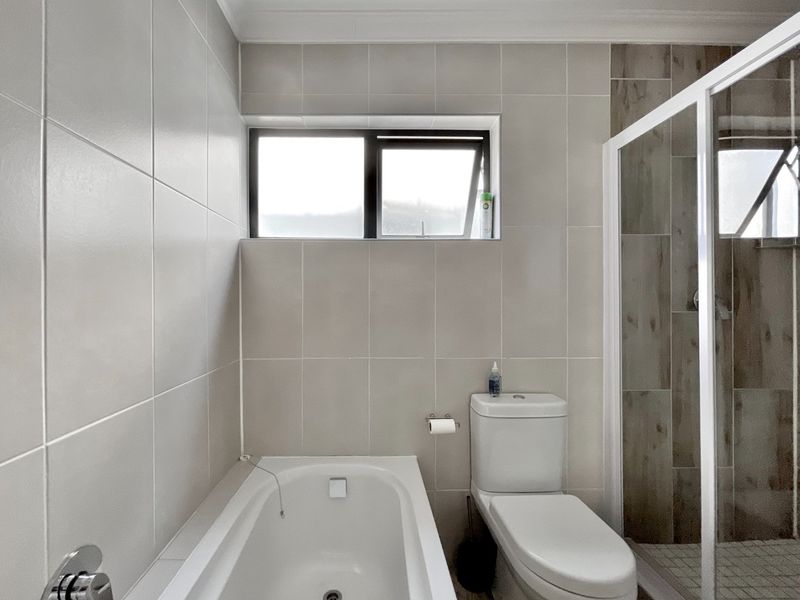 A modern bathroom featuring a built-in bathtub, a separate shower enclosure with tiled accents, and a toilet, finished with neutral wall tiles.