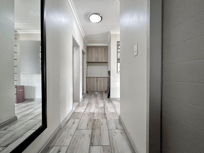 A clean, well-lit hallway featuring wood-look tile flooring and built-in cabinetry at the end, providing a neutral and functional transition space.