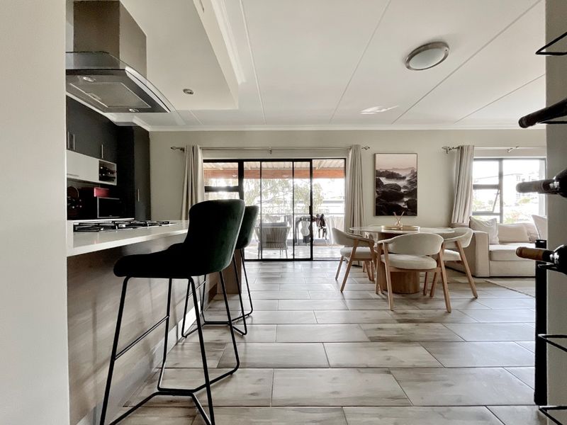 Modern open-plan living area featuring a sleek kitchen with stone countertops, gas hob, and tiled flooring, flowing seamlessly to an outdoor patio space.