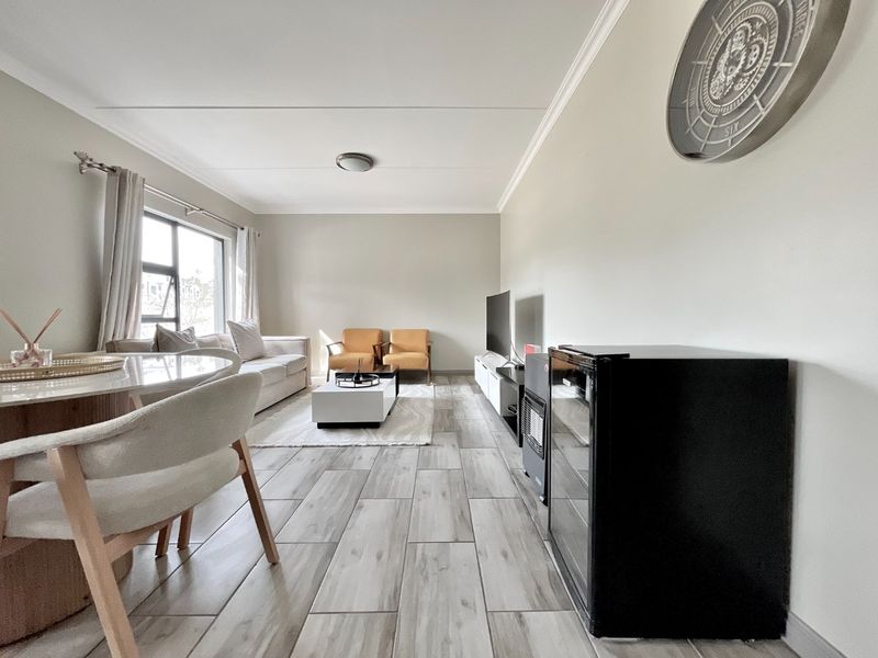 A bright and modern open-plan living area featuring contemporary wood-look tiled flooring and neutral wall finishes.